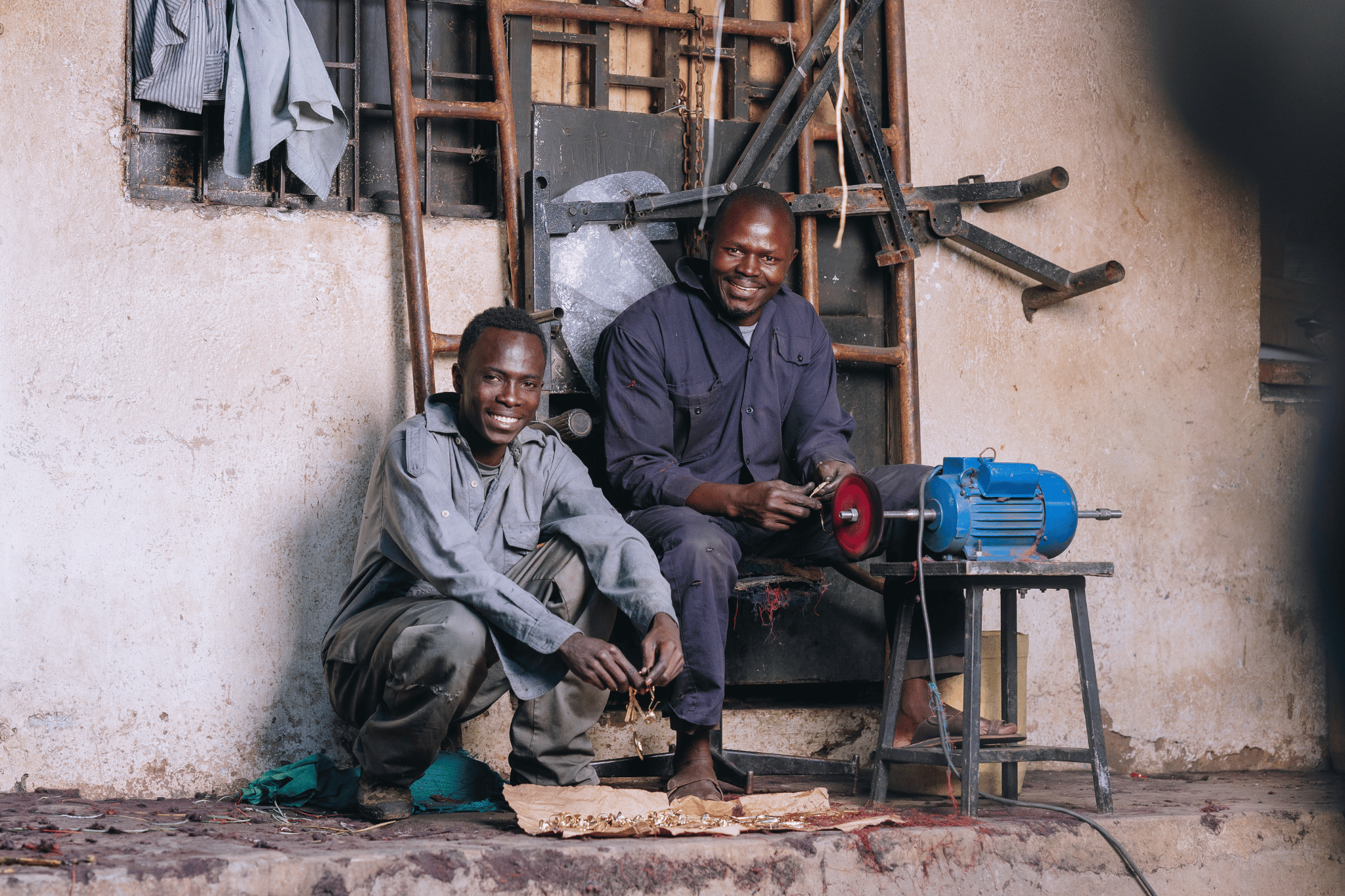 Two men sitting in a workshop with tools and equipment.