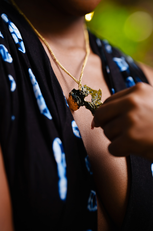 Model wearing a gold chain necklace with a gold hammered pendant of the African Continent with a heart cut out. 