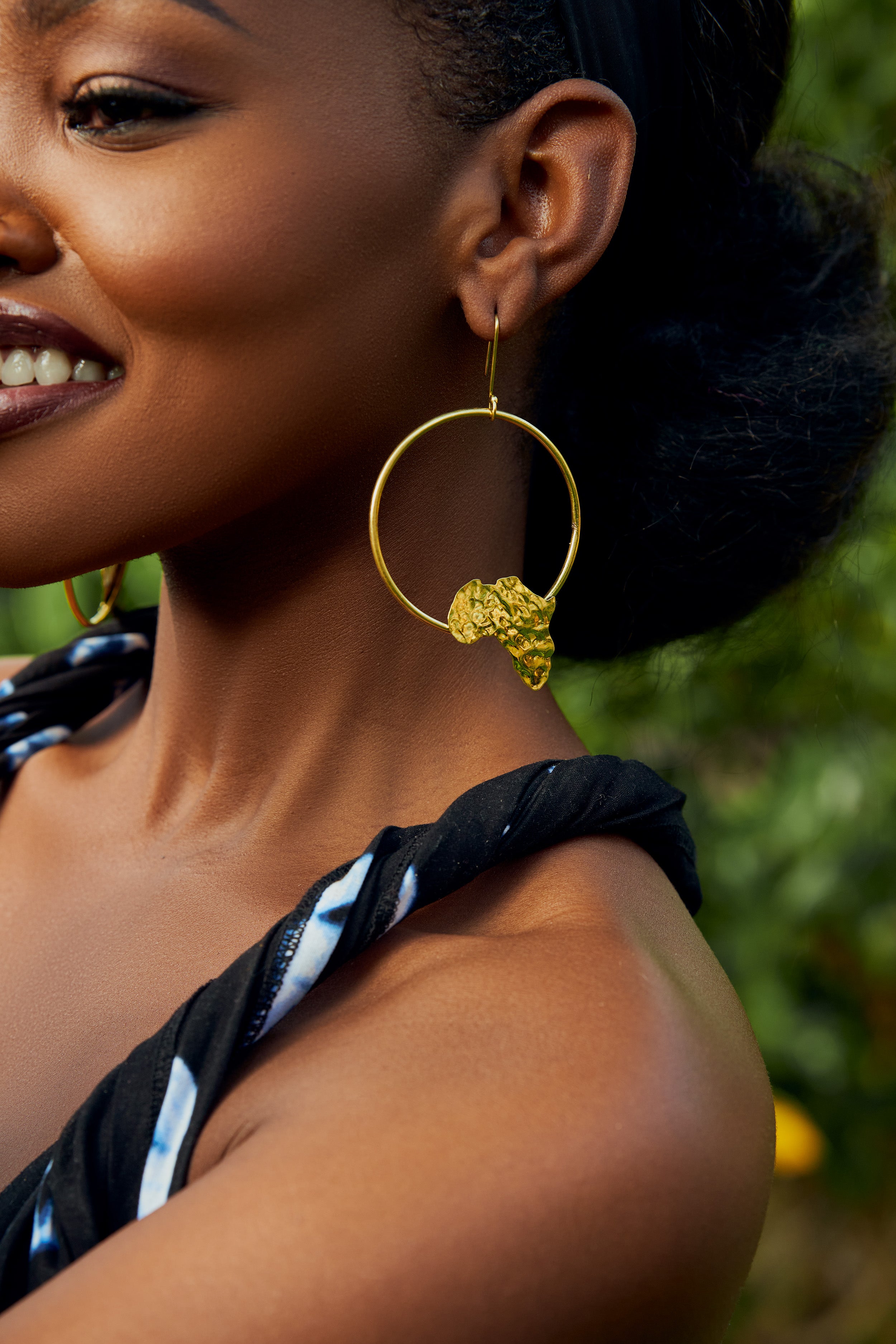 Model wearing gold hoop earrings with an  africa map shape accent on the bottom part of the hoop