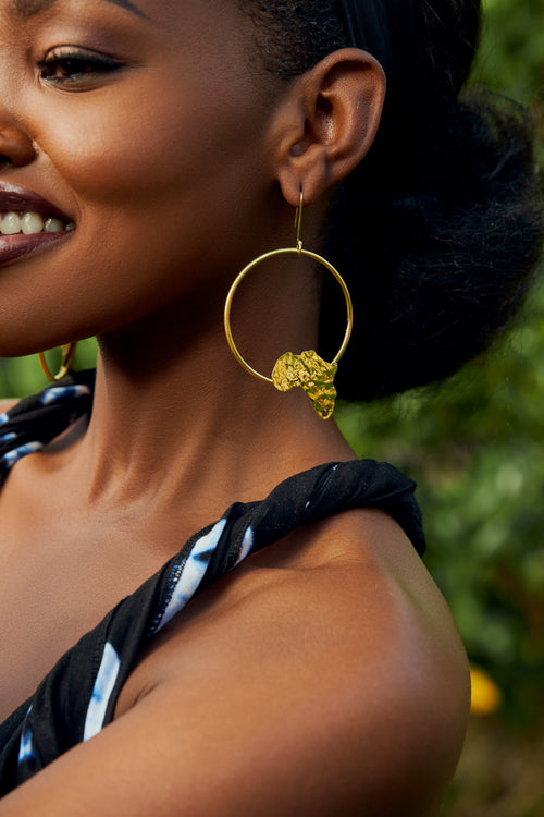 Model wearing gold hoop earrings with an  africa map shape accent on the bottom part of the hoop