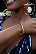 Close-up of a model' arm wearing a gold bracelet with gold and white hoop earrings.