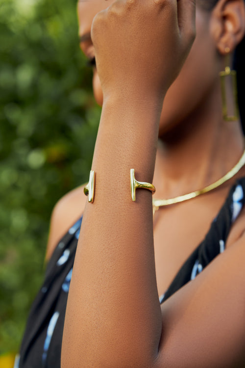 Close up of a model's wrist wearing a gold bracelet with an open-ended design with asymmetrical contours. 