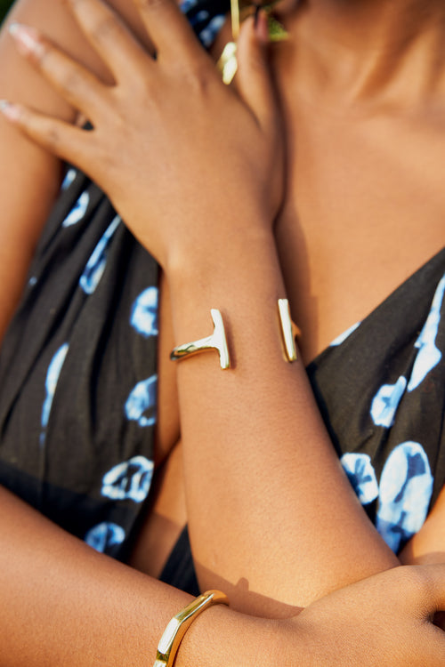 Close up of a model's wrist wearing a gold bracelet with an open-ended design with asymmetrical contours. 