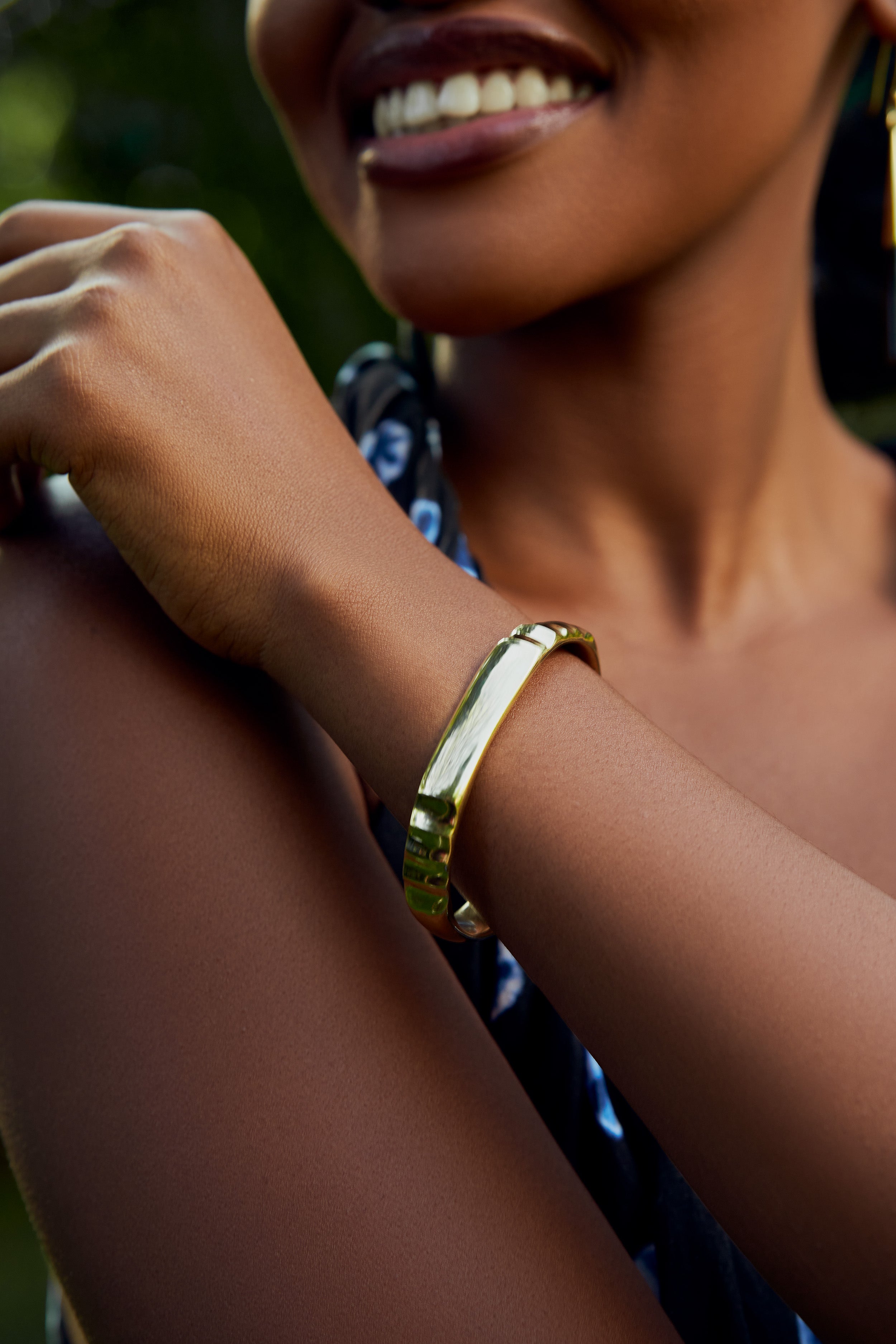 Close-up of a model wearing a gold contoured bracelet with a blurred background