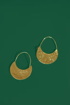 Gold crescent shaped earrings on a green background
