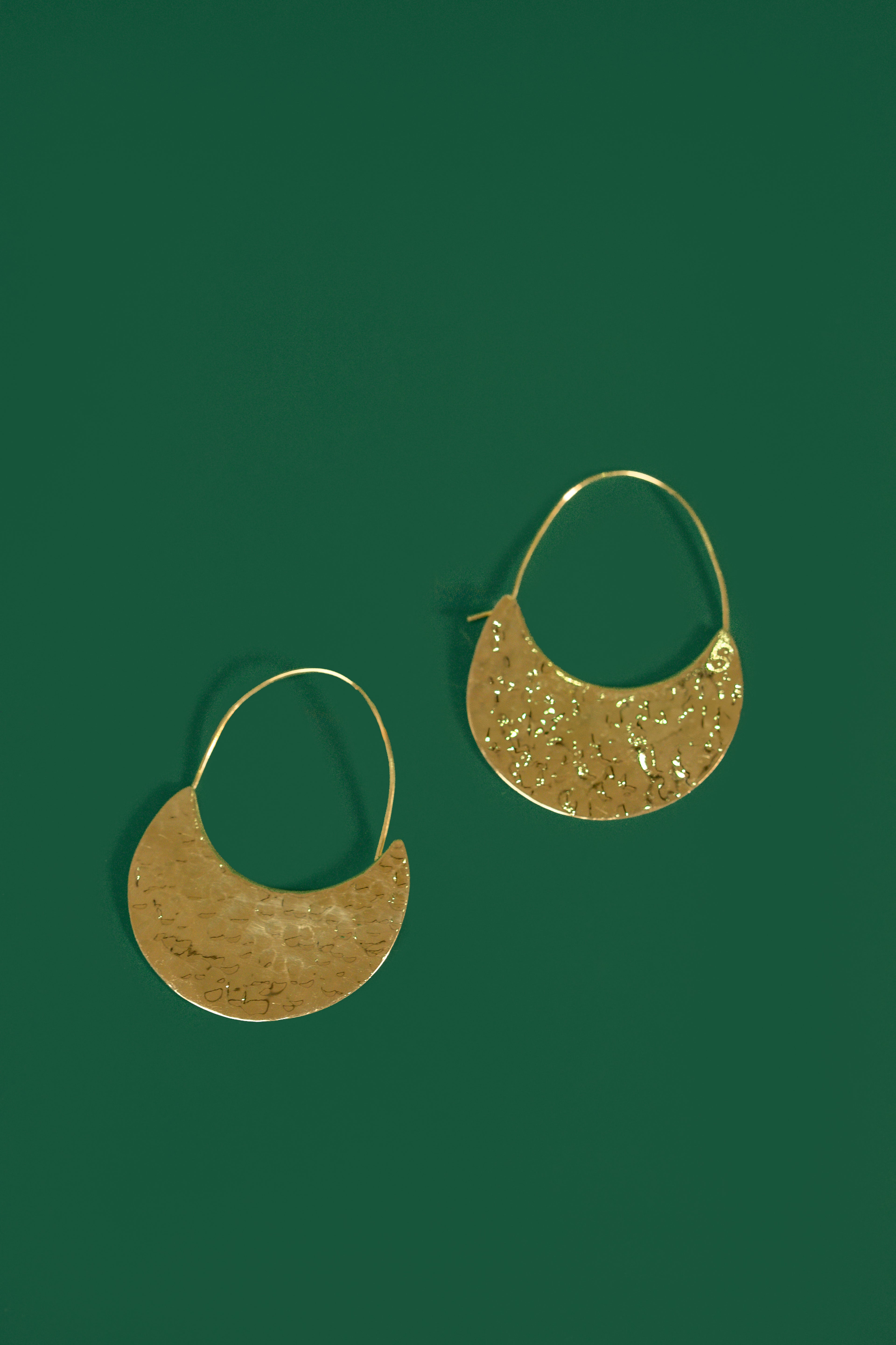 Gold crescent shaped earrings on a green background