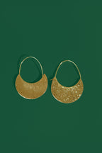 Gold crescent shaped earrings on a green background