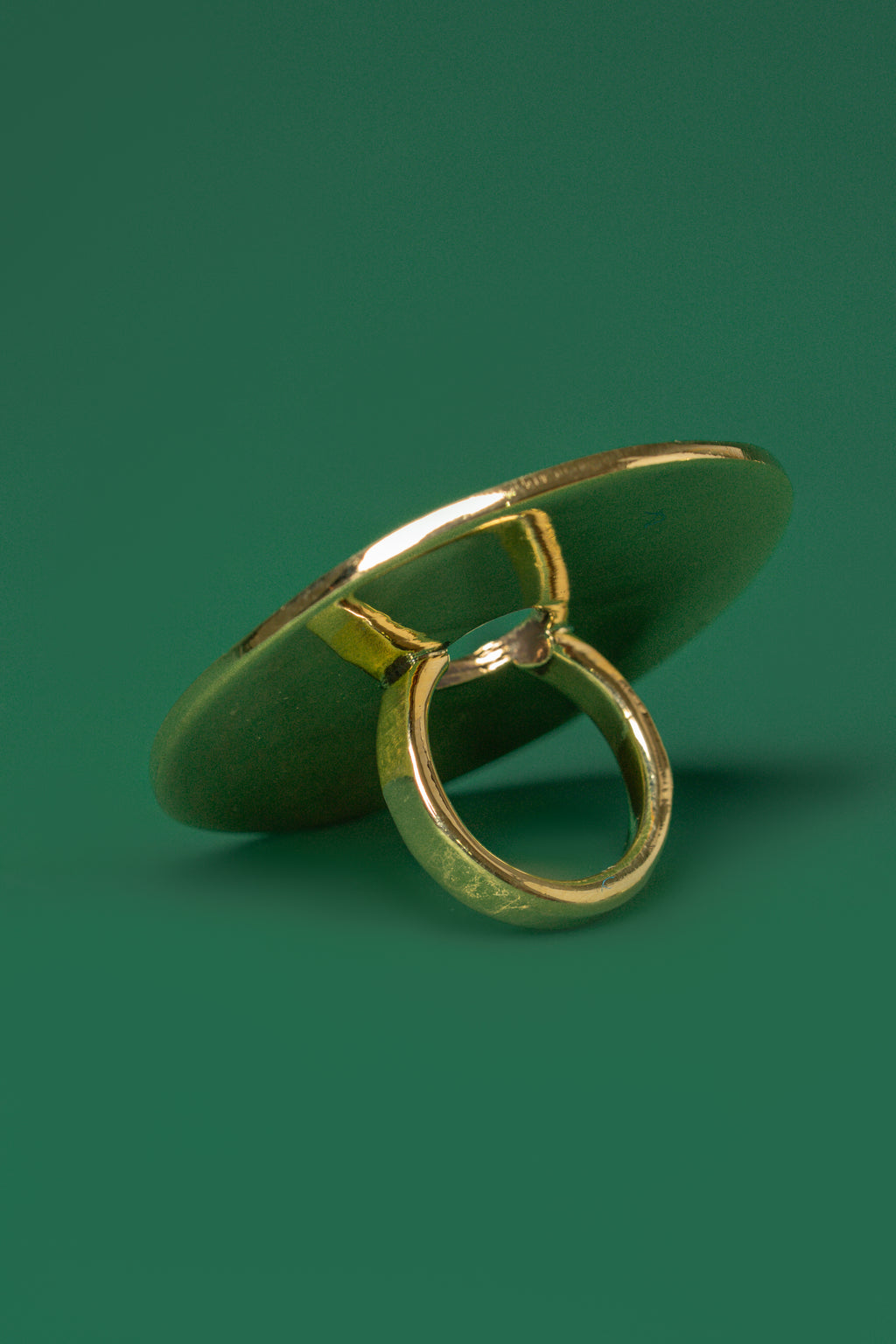 A gold flat circular disc shaped ring on a green flat background.