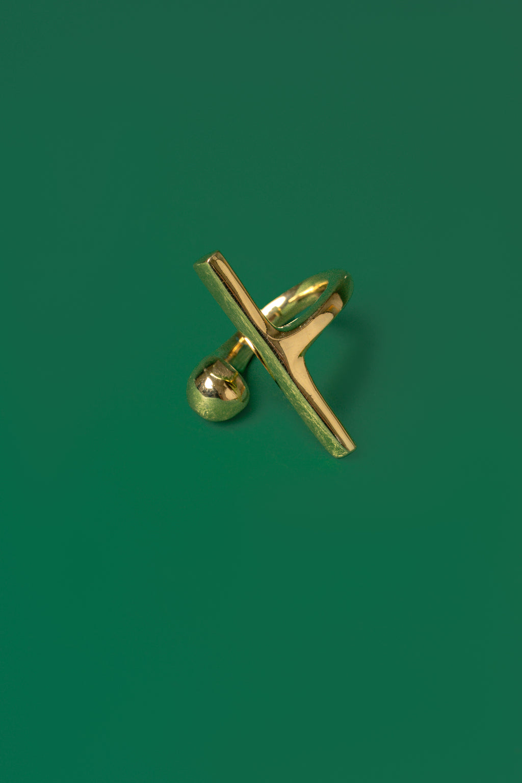 A gold open band ring with a sphere motif and a sleek bar design on a green flat background.