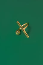 A gold open band ring with a sphere motif and a sleek bar design on a green flat background.