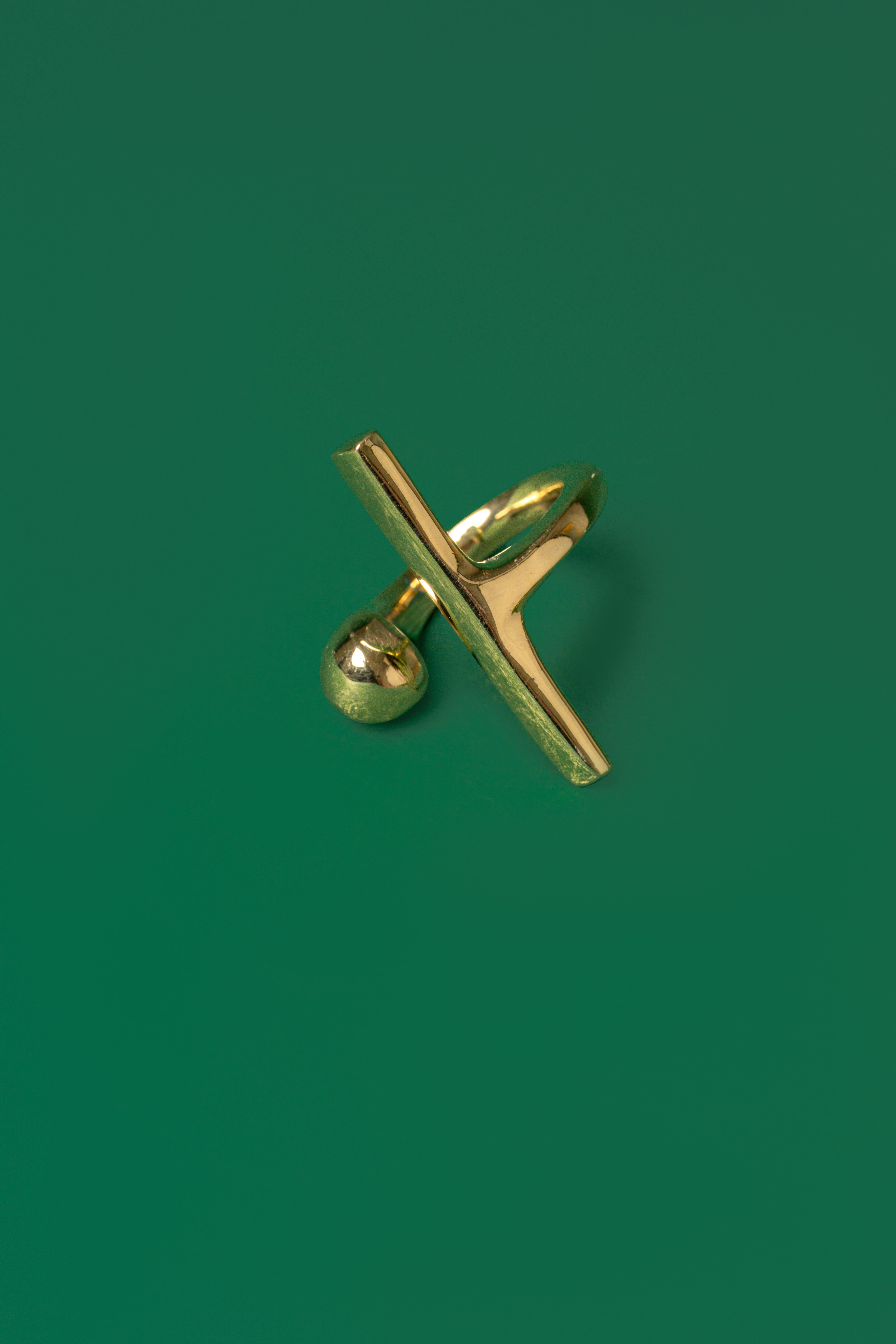 A gold open band ring with a sphere motif and a sleek bar design on a green flat background.
