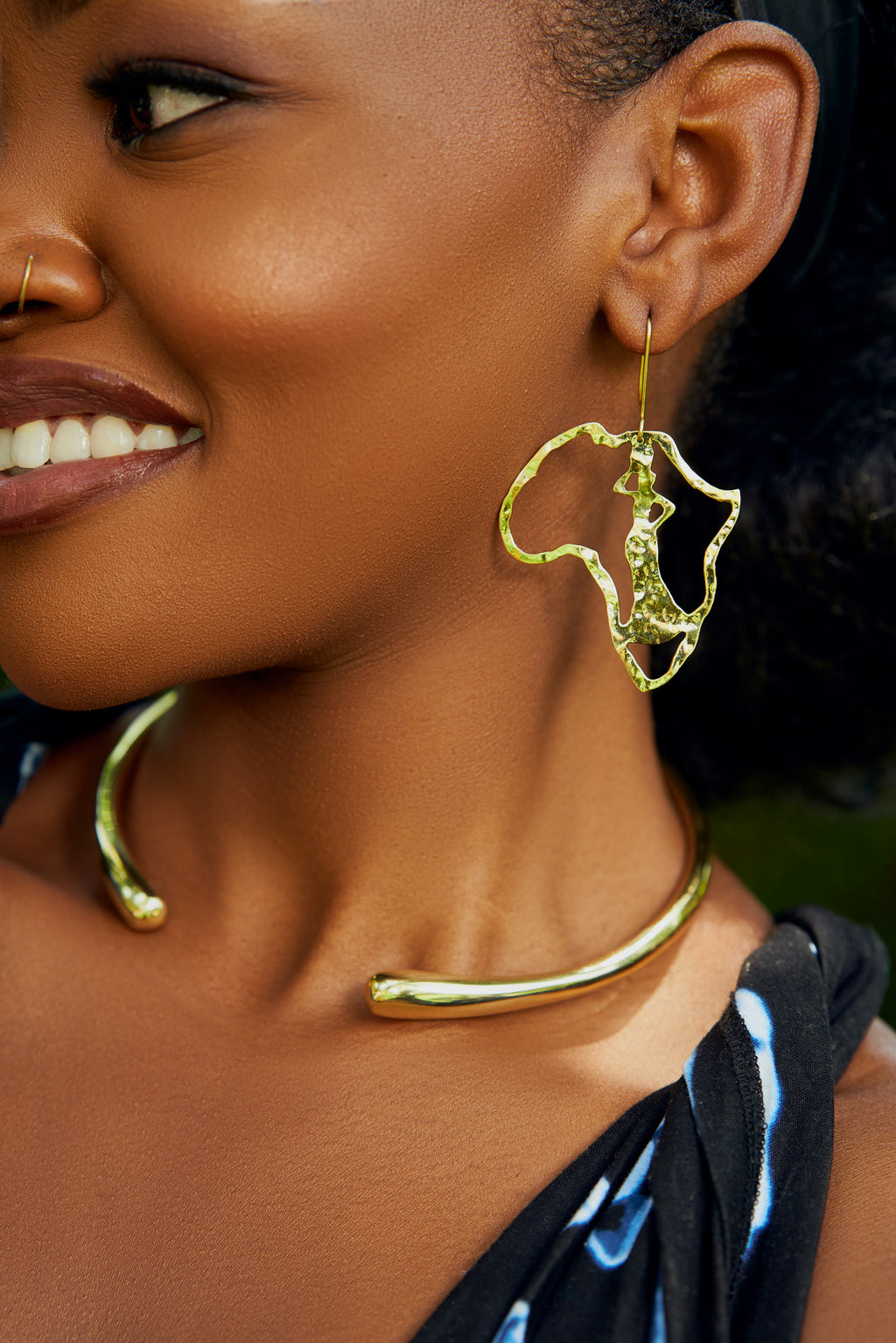Model wearing gold Africa map outline  shaped dangle earrings with a standing female figure cut out inside inside. 