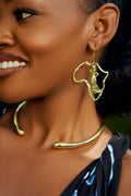 Model wearing gold Africa map outline  shaped dangle earrings with a standing female figure cut out inside inside. 
