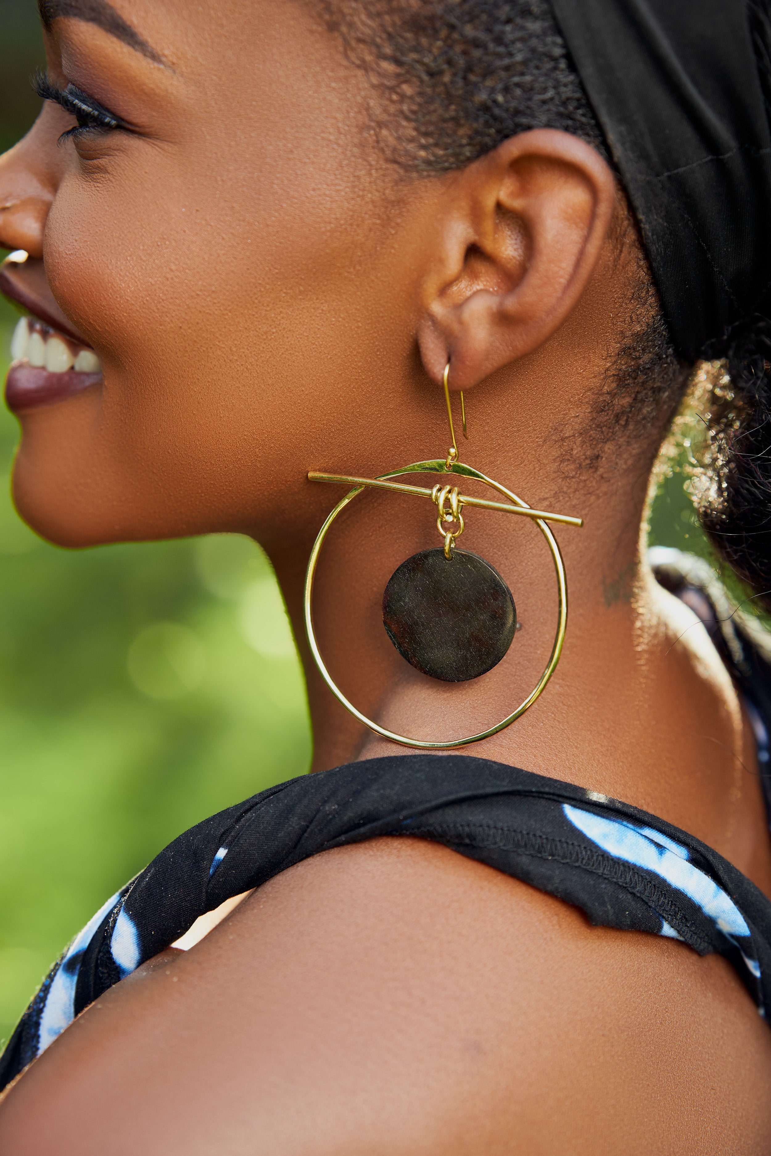 Model wearing large gold hoop earrings with a black circular disk in the center