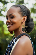 Model wearing large gold hoop earrings with a black circular disk in the center