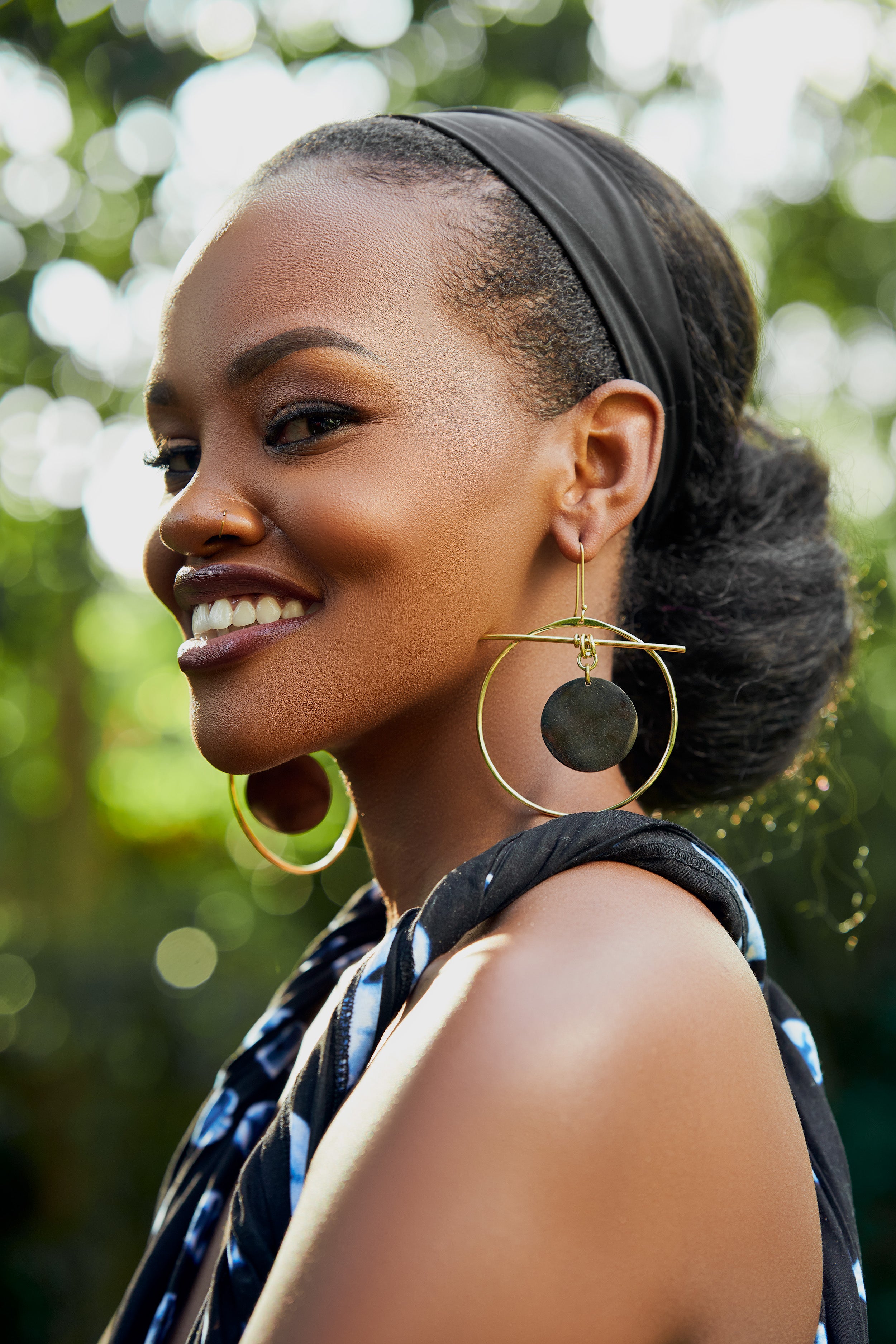 Model wearing large gold hoop earrings with a black circular disk in the center
