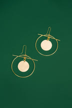 Gold hoop earrings with white circular discs on a green background