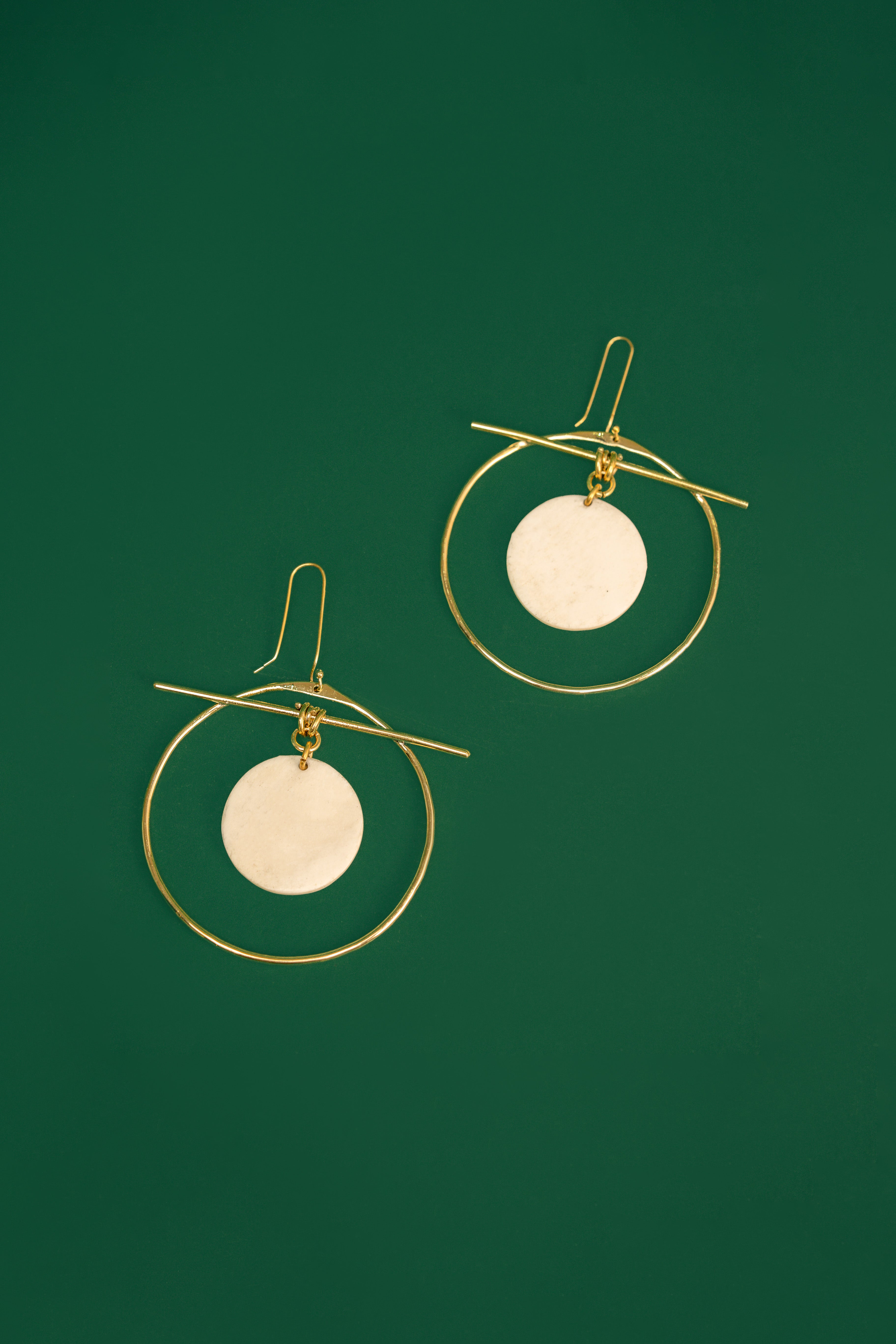 Gold hoop earrings with white circular discs on a green background