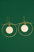 Gold hoop earrings with white circular discs on a green background