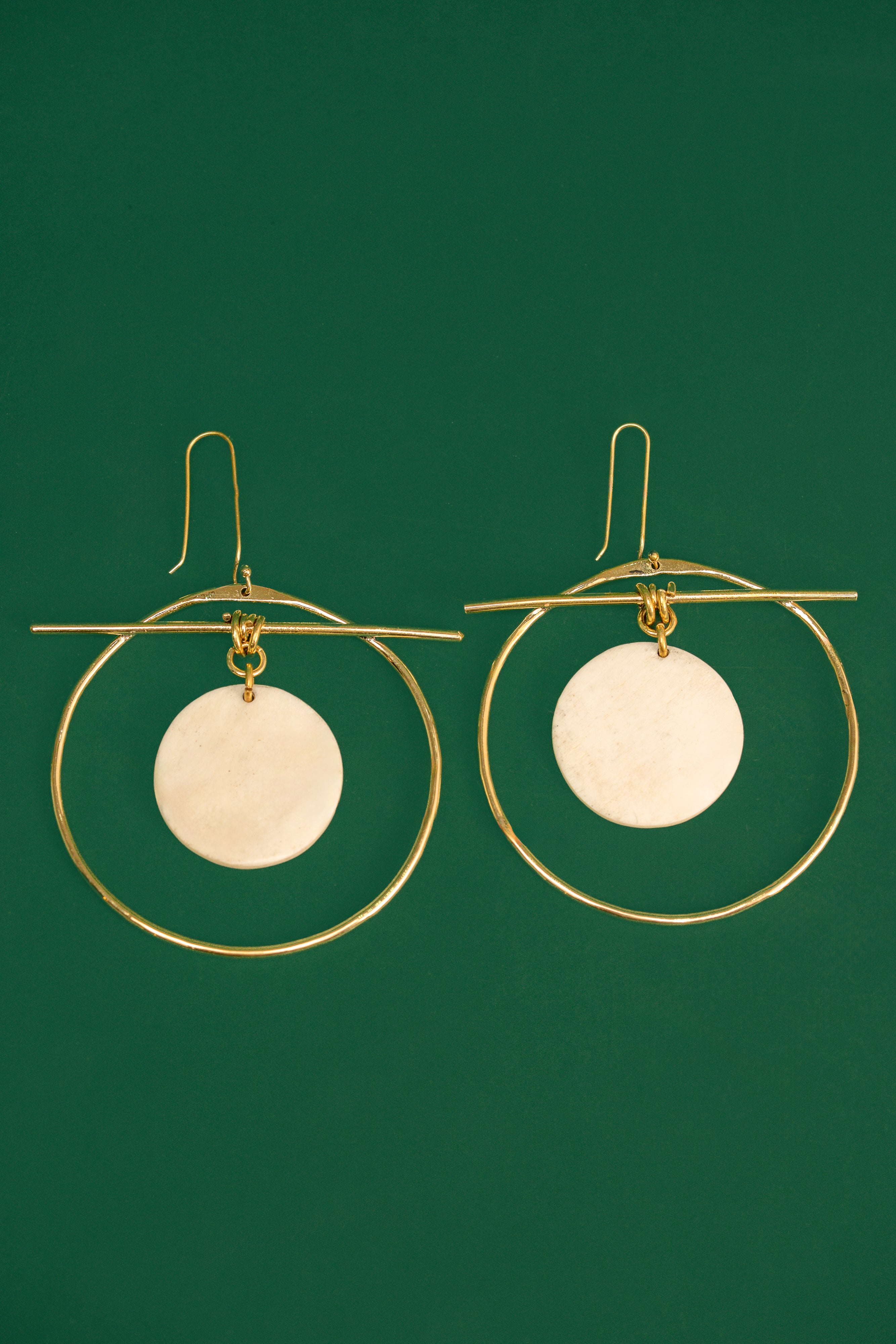Gold hoop earrings with white circular discs on a green background