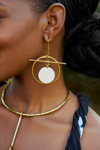 Model wearing large gold hoop earrings with a white circular disk in the center