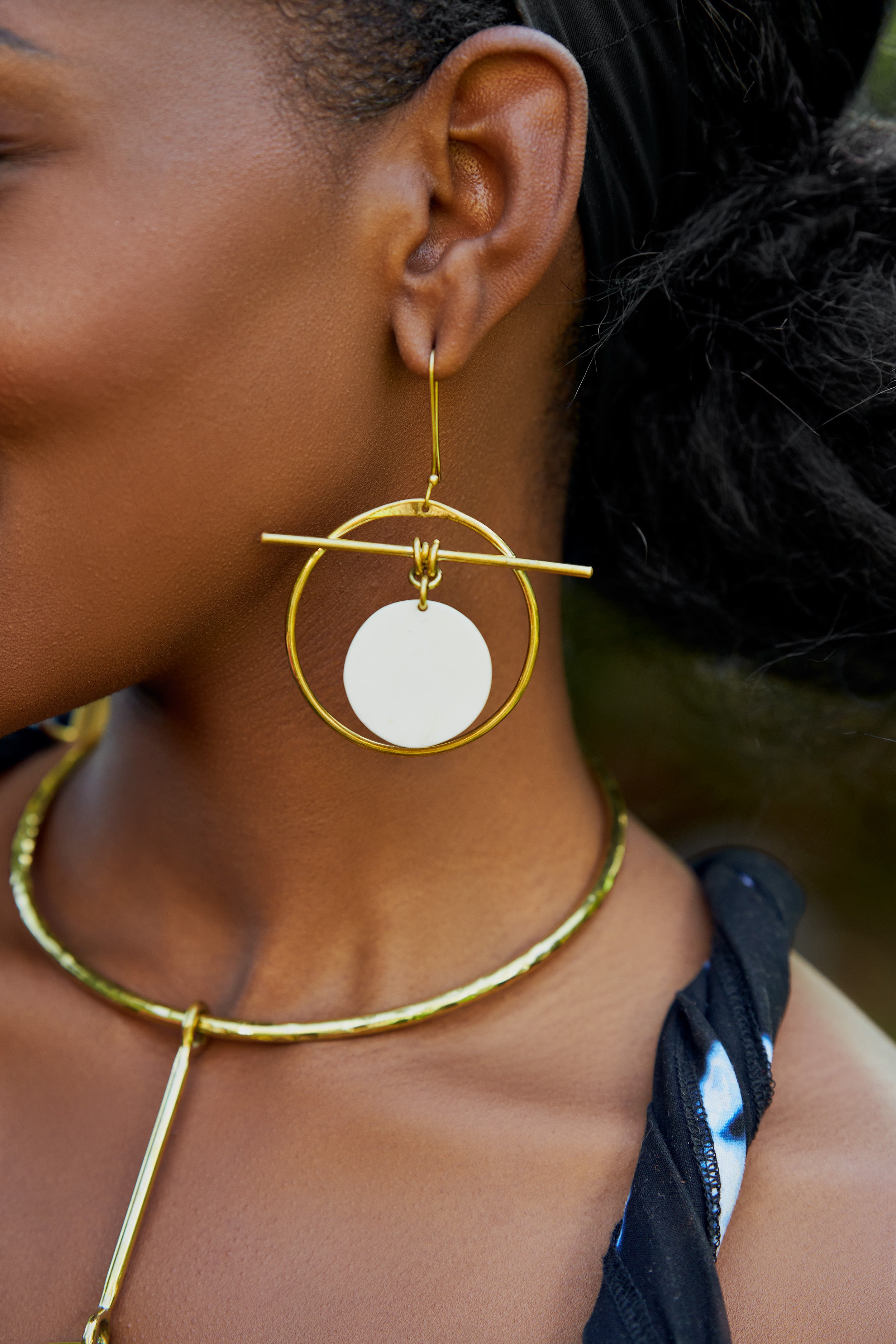 Model wearing large gold hoop earrings with a white circular disk in the center