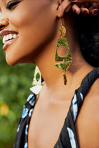 Model wearing gold earrings with geometric shapes cut out pendants