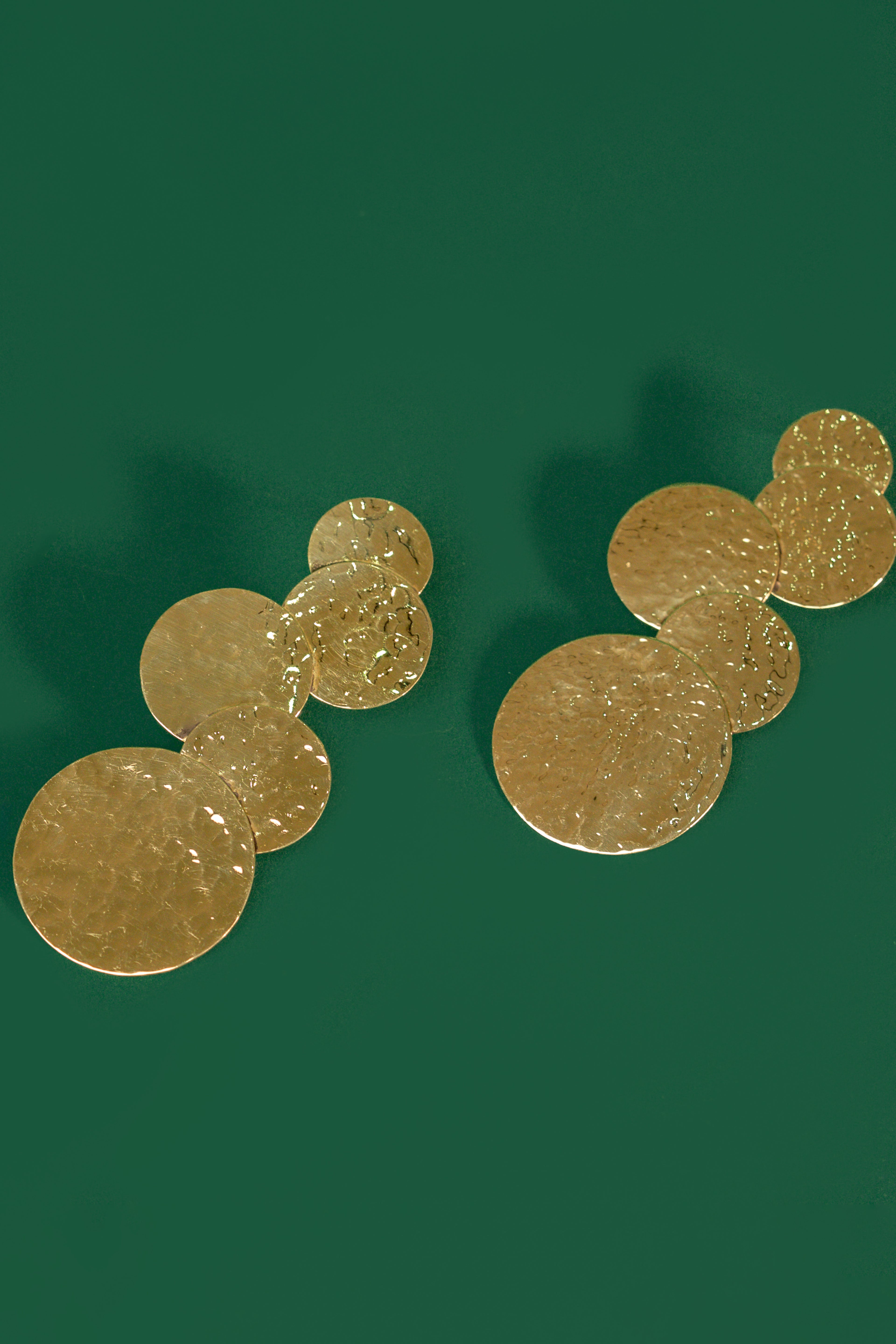 A pair of gold cascading circular earrings on a green background