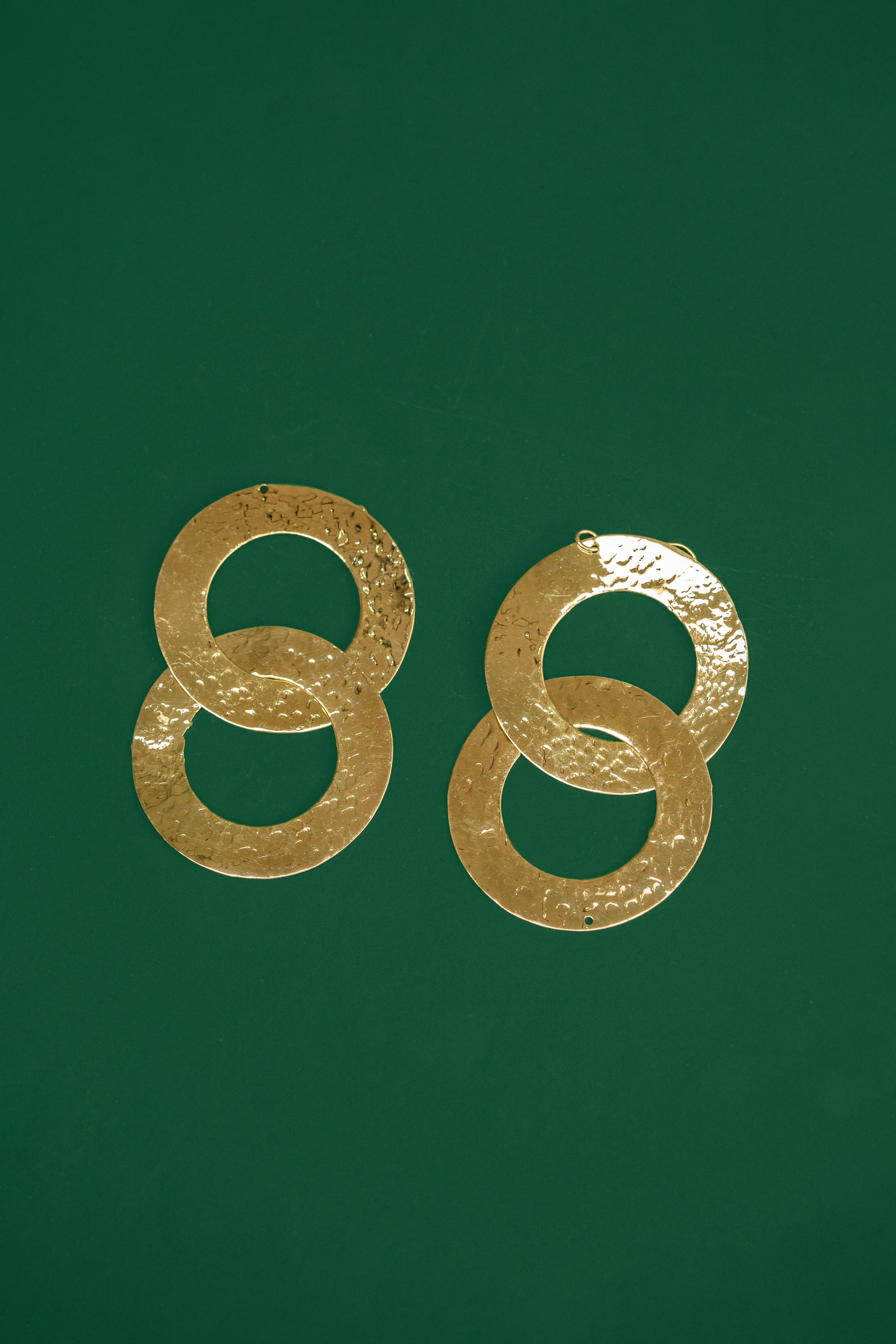 Pair of gold double interlocking hoop earrings on a green background