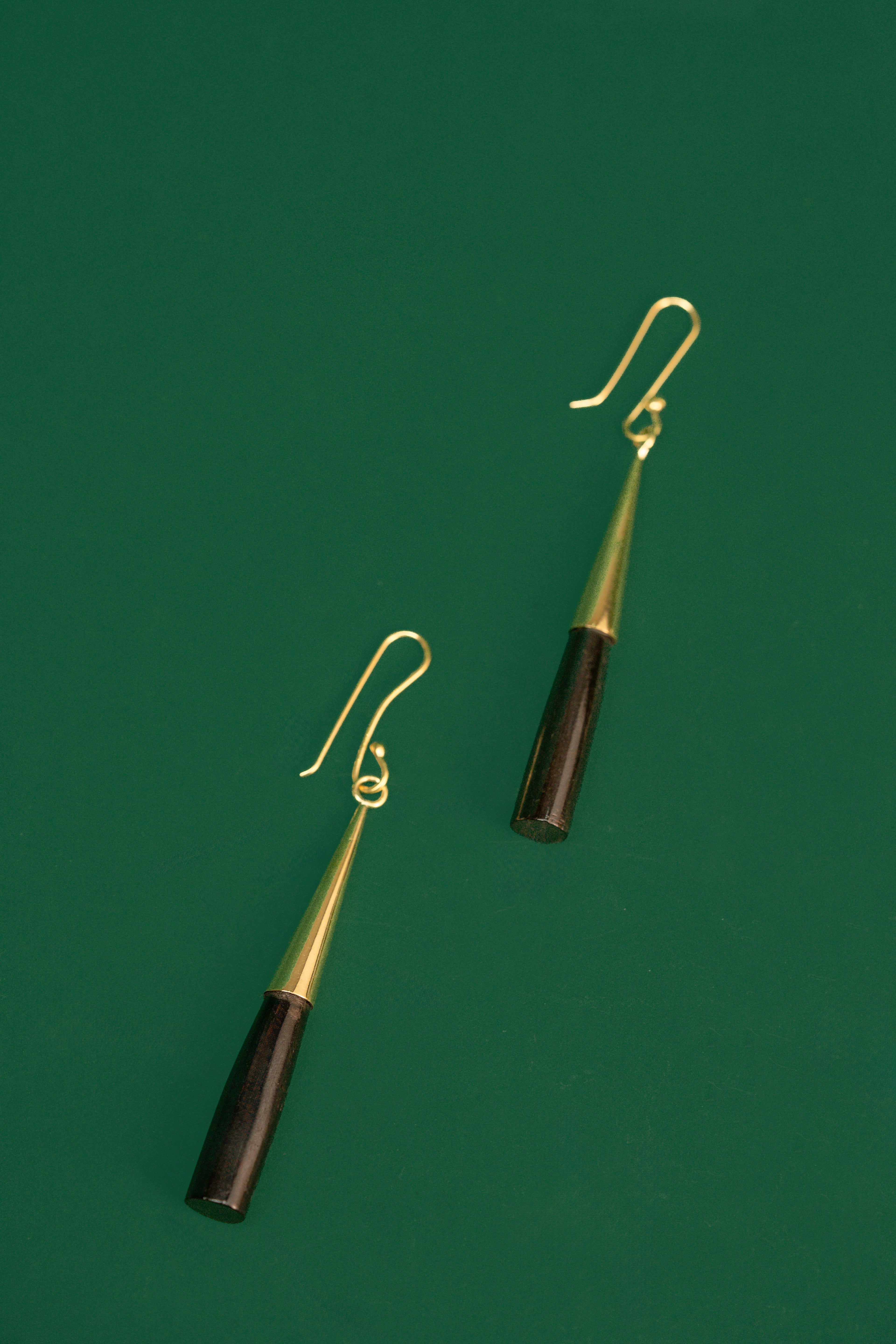 Pair of earrings with black and gold cylindrical design on a green background