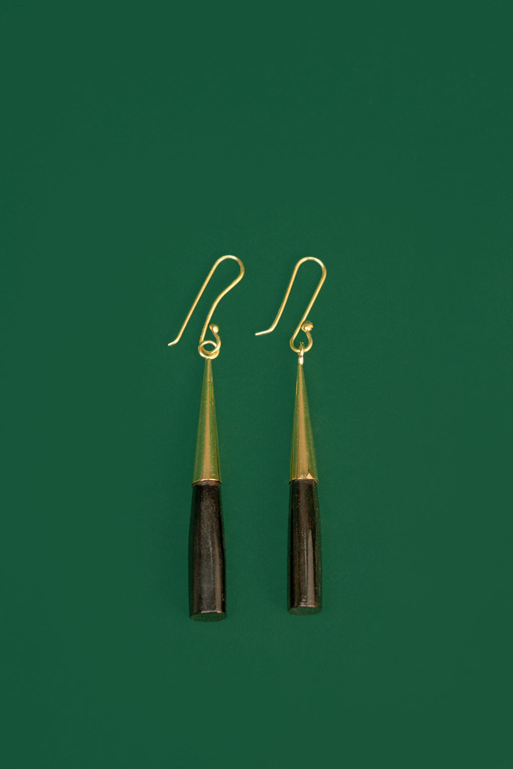 Pair of earrings with black and gold cylindrical design on a green background