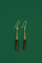 Pair of earrings with black and gold cylindrical design on a green background