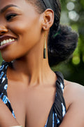 Model wearing black and gold cylindrical bar dangle earrings. 