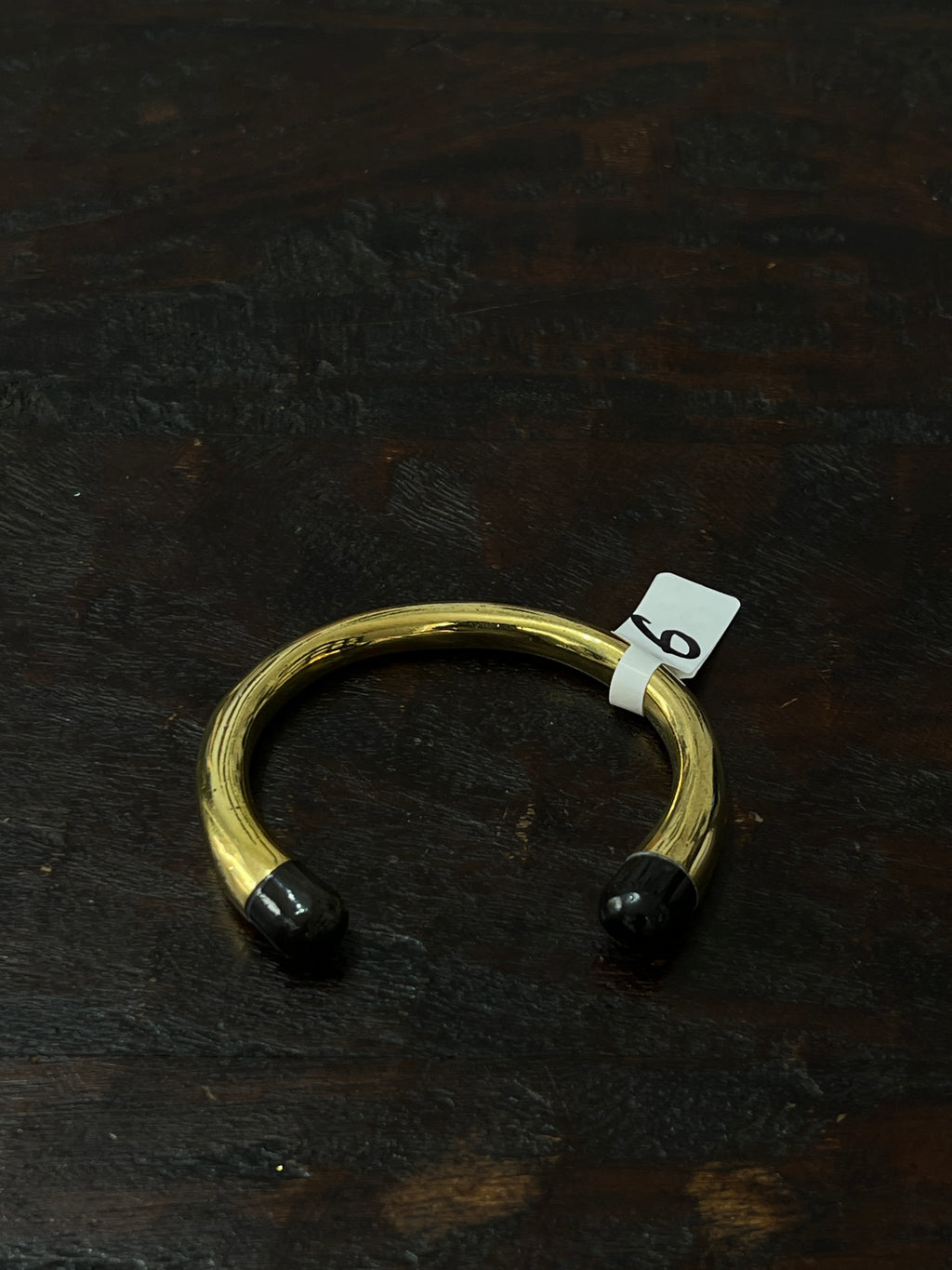 Gold bracelet with black ends on a dark wooden surface
