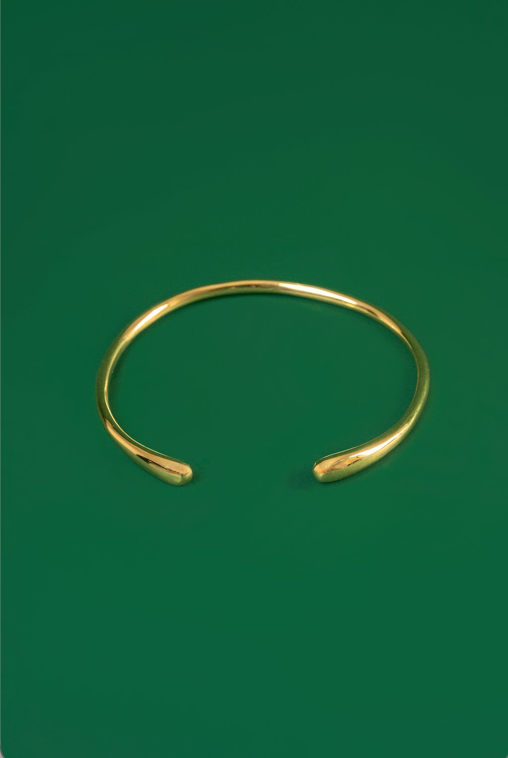 A polished gold open ended choker with tear drop shaped ends displayed on a solid dark green background.