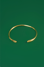 A polished gold open ended choker with tear drop shaped ends displayed on a solid dark green background.