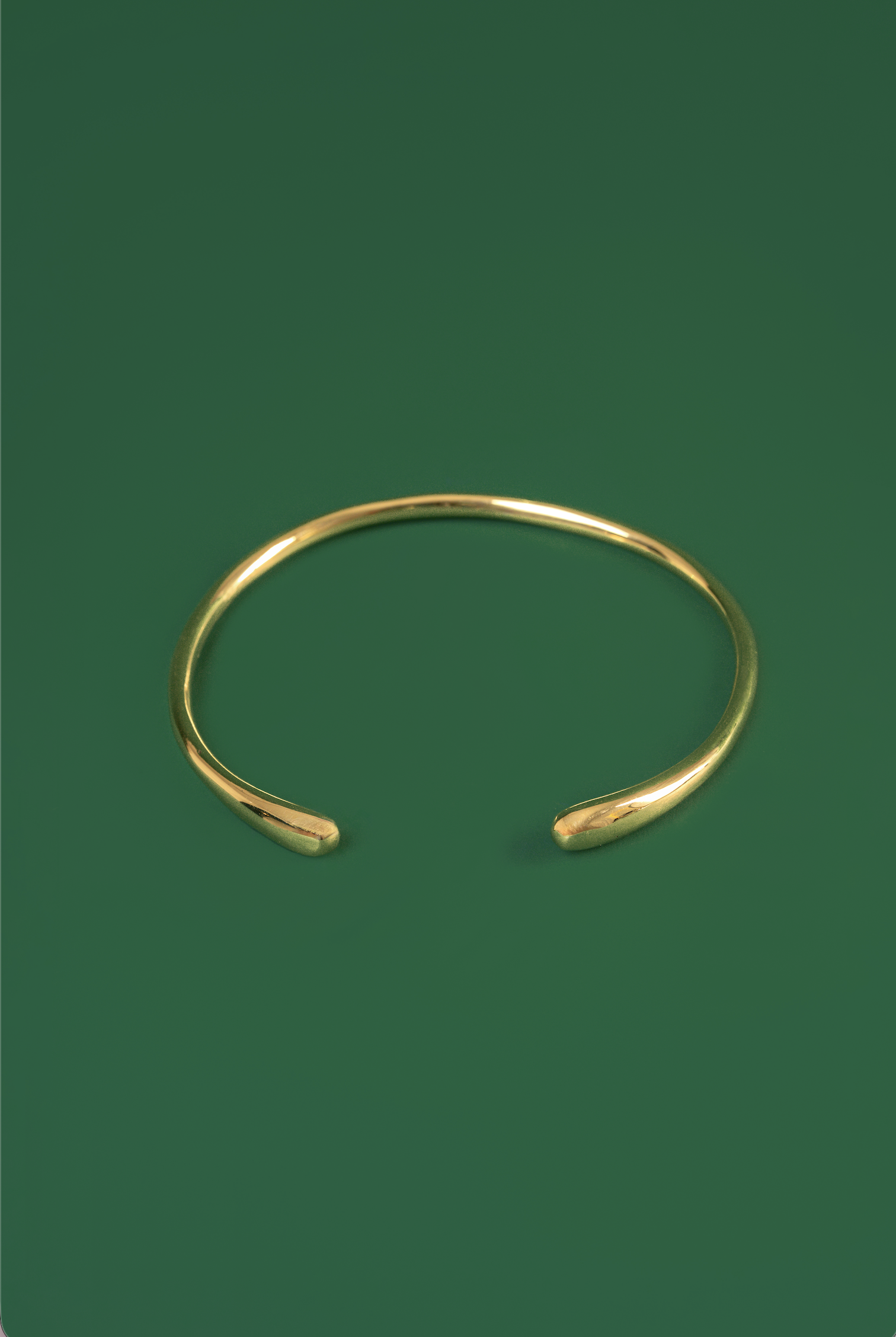 A polished gold open ended choker with tear drop shaped ends displayed on a solid dark green background.