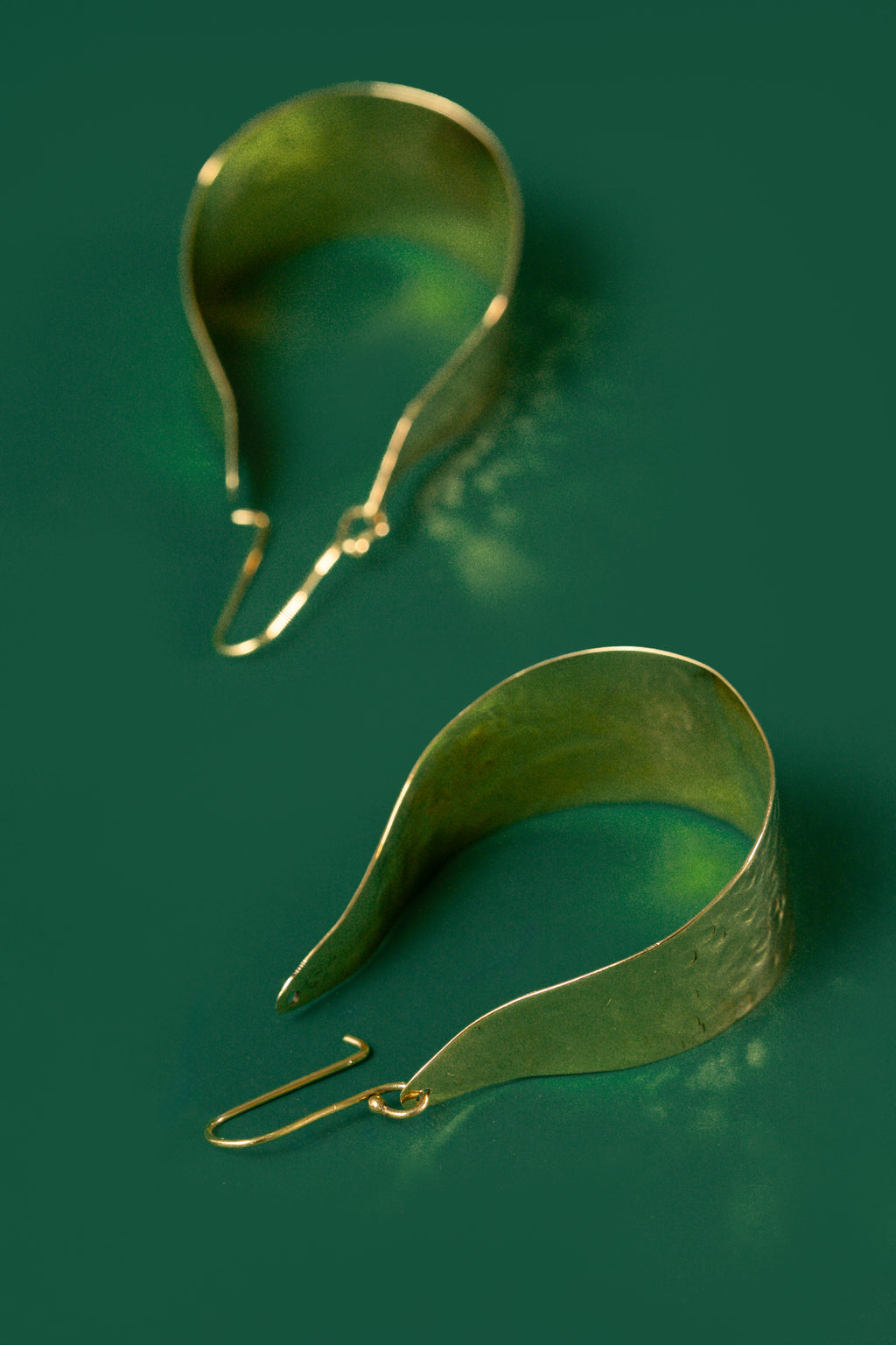 Gold drop shaped earrings on a green background