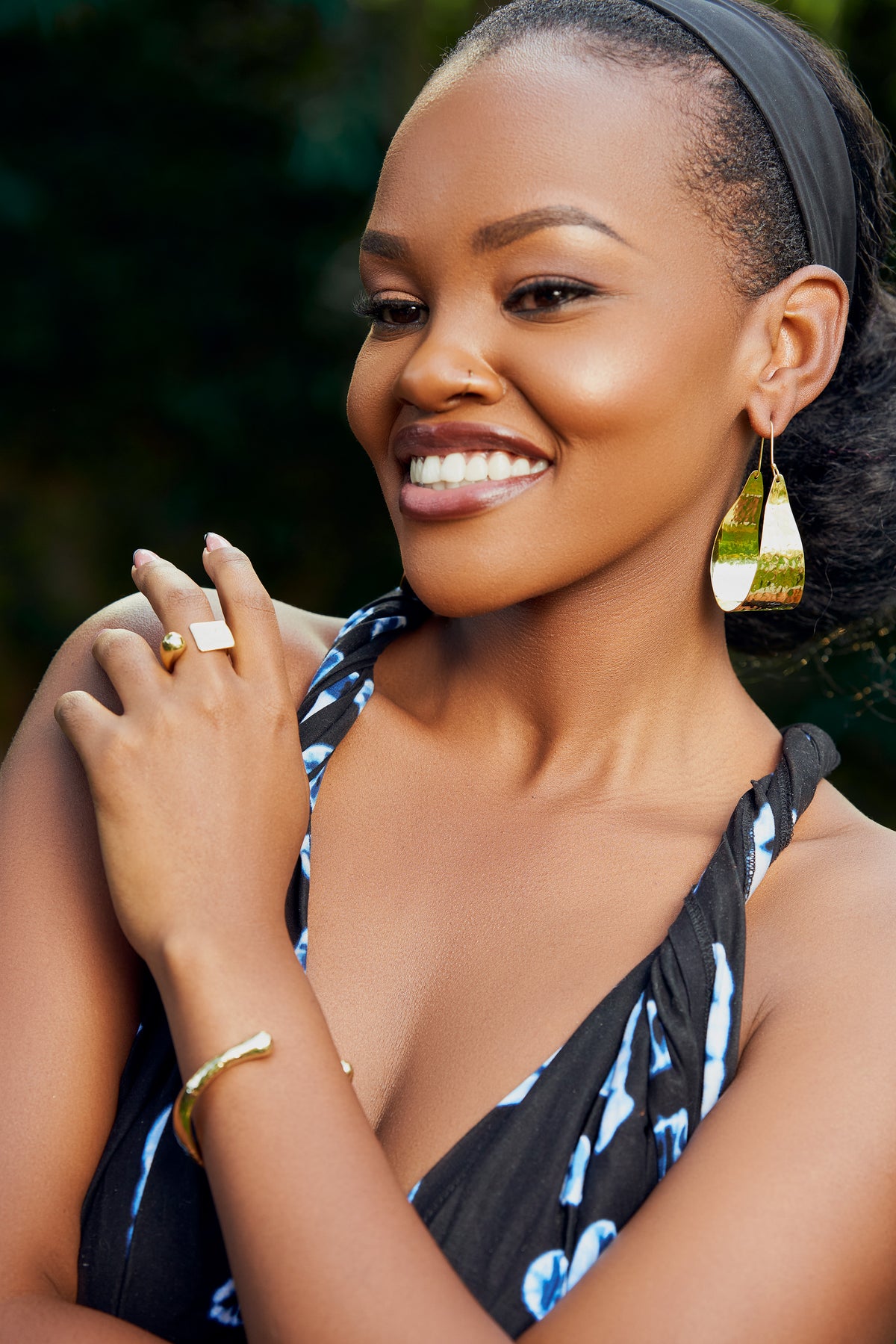 Woman wearing gold tear drop shaped earrings and a square ring. 