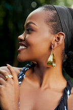 Woman wearing gold tear drop shaped earrings and a square ring. 