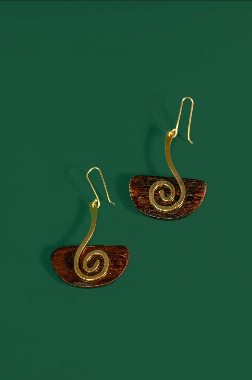 A pair of spiral drop earrings with gold-toned wire spirals and brown semicircular discs, shown on a solid dark green background.