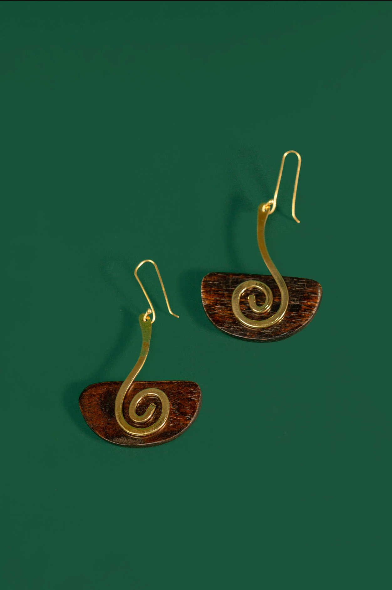 A pair of spiral drop earrings with gold-toned wire spirals and brown semicircular discs, shown on a solid dark green background.