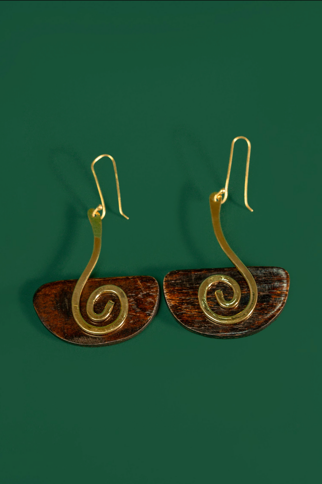 A pair of spiral drop earrings with gold-toned wire spirals and brown semicircular discs, shown on a solid dark green background.