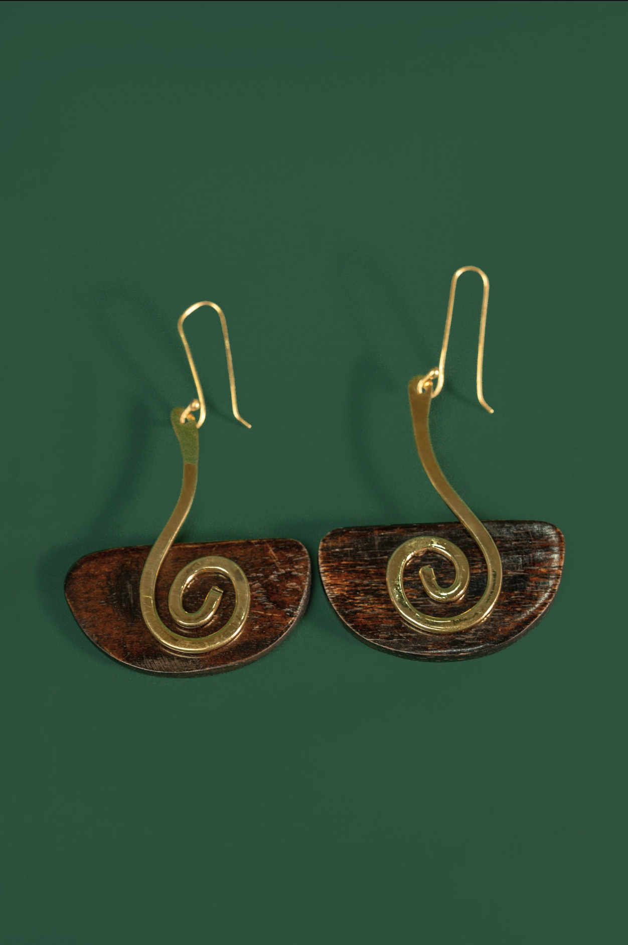 A pair of spiral drop earrings with gold-toned wire spirals and brown semicircular discs, shown on a solid dark green background.