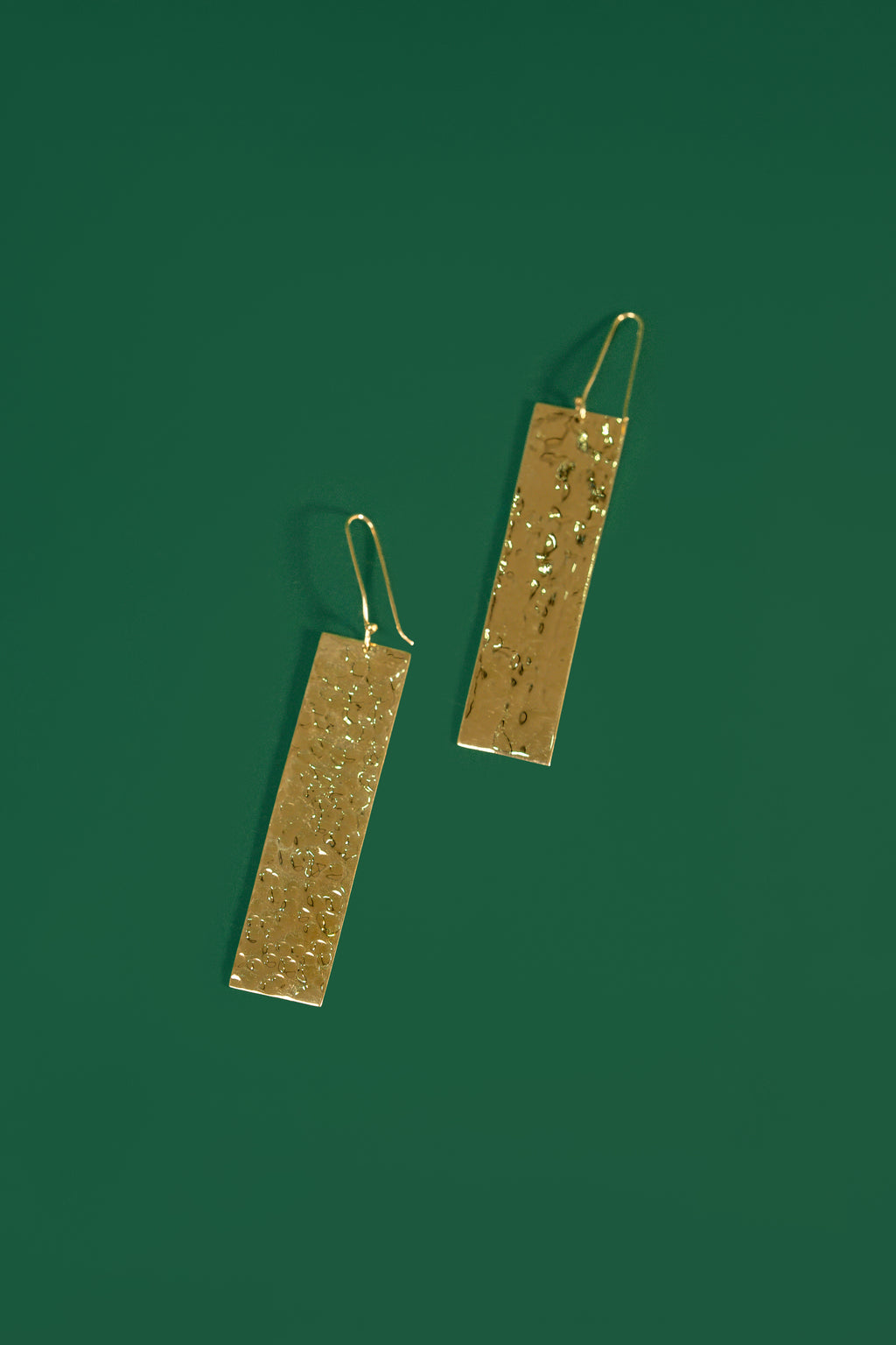Gold rectangular earrings on a green background