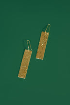 Gold rectangular earrings on a green background