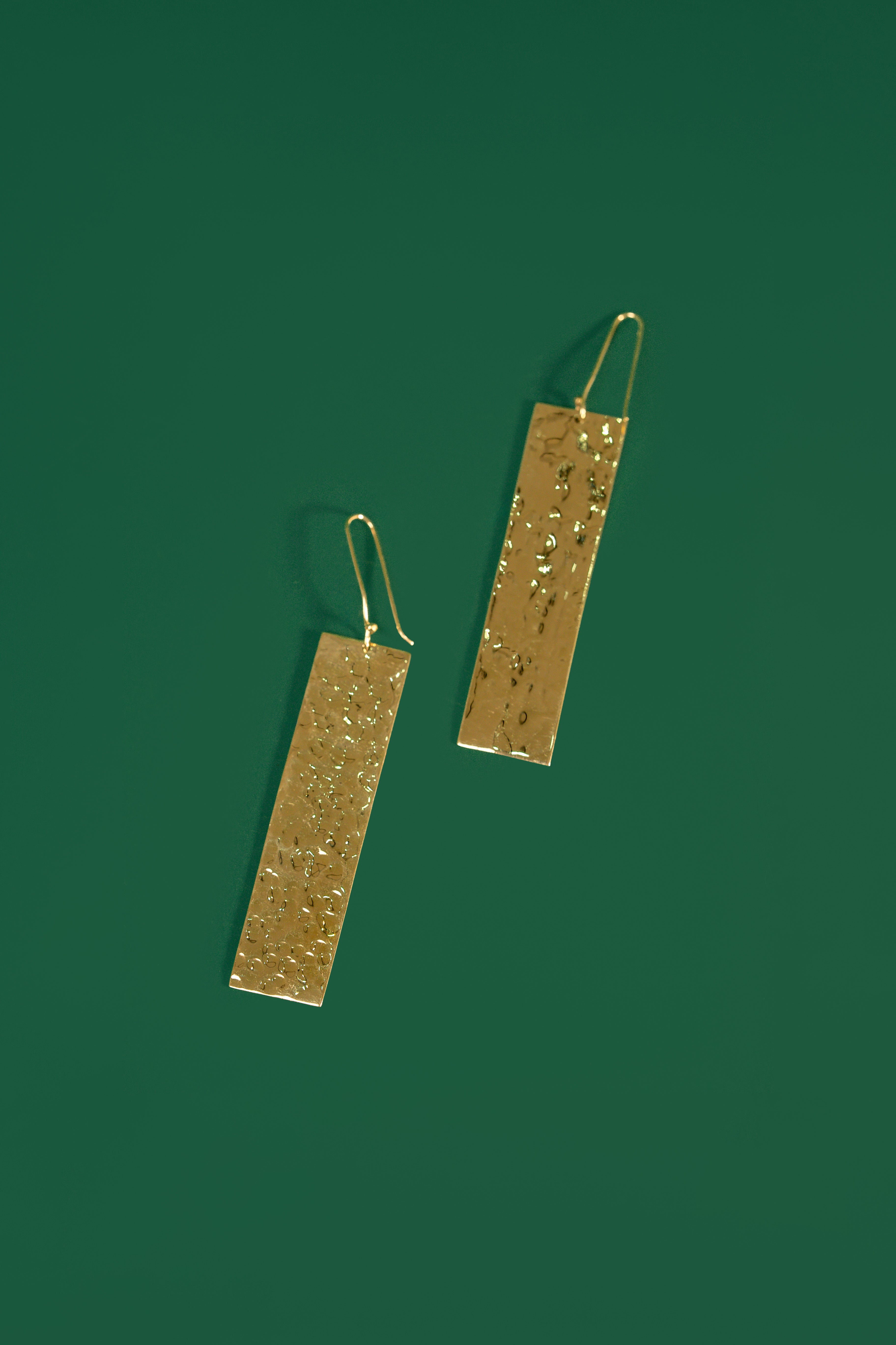 Gold rectangular earrings on a green background