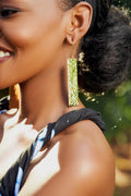 Model wearing gold rectangular earrings with a blurred green background