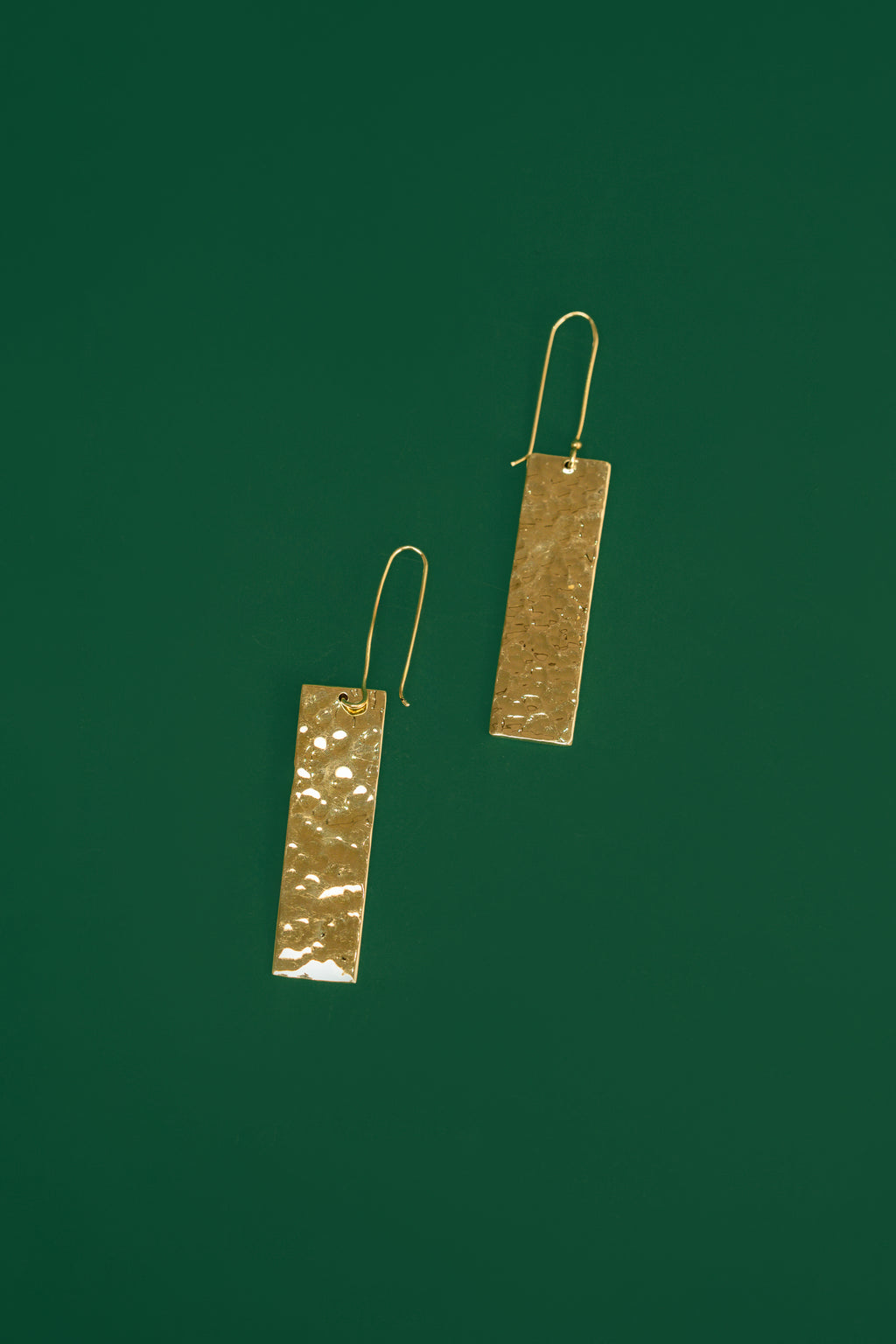 Pair of gold rectangular earrings on a green background