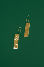 Pair of gold rectangular earrings on a green background